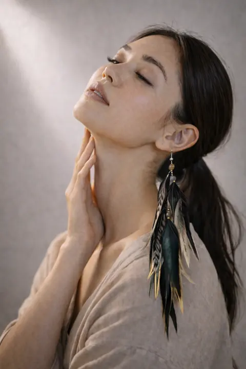 AI model with eyes closed wearing a black and teal feather earring